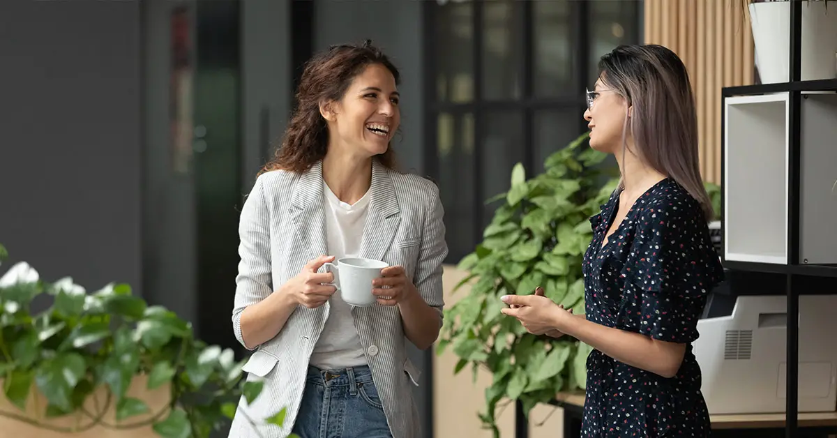 2 women chatting at work. One woman holding a cup of coffee