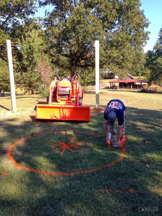 Man spraying the area on his lawn with orange spray paint to accurately place the pergola. 