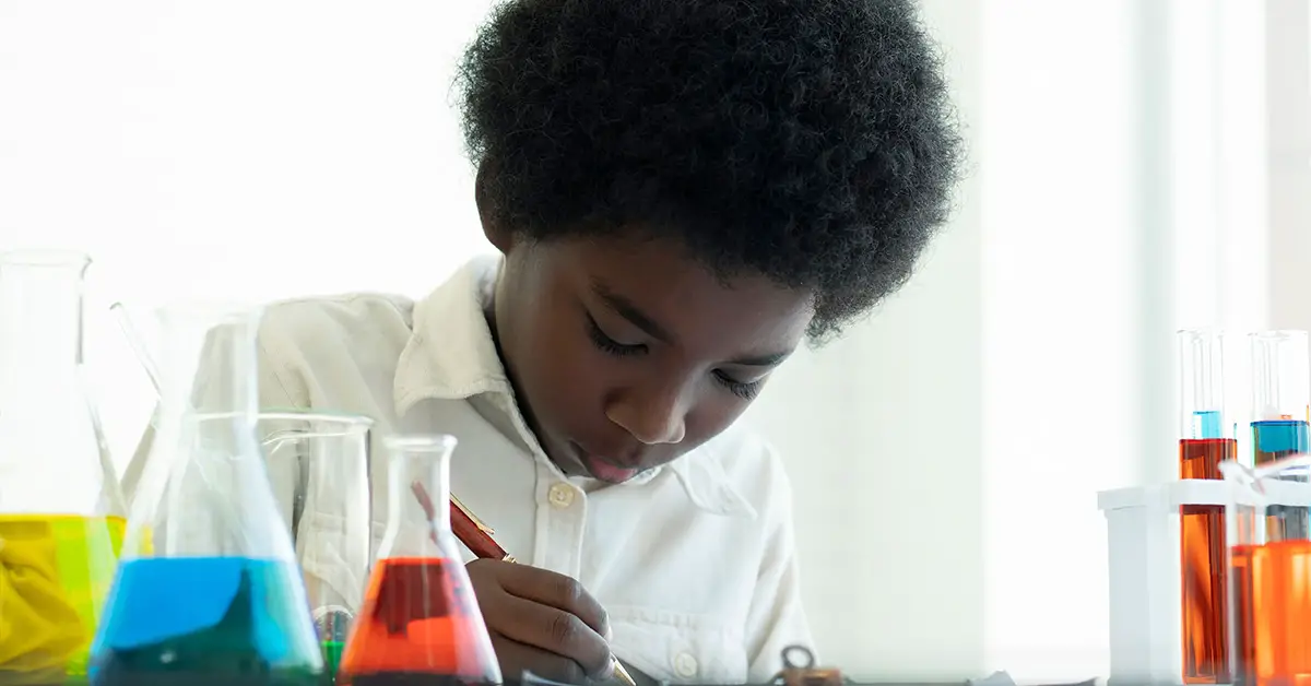 young person working in a scientific setting with beakers filled with various different coloured liquids