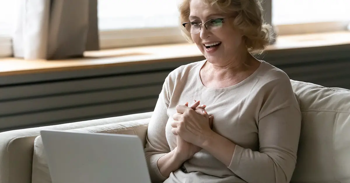 woman clasping hands in delight while using laptop