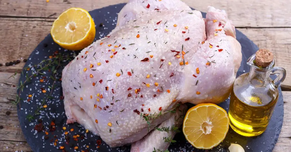 whole raw chicken with thyme, chili flakes, lemon and olive oil