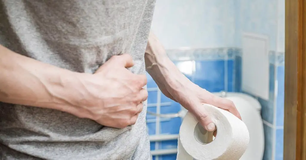 person holding lower abdomen in discomfort while holding toilet paper roll