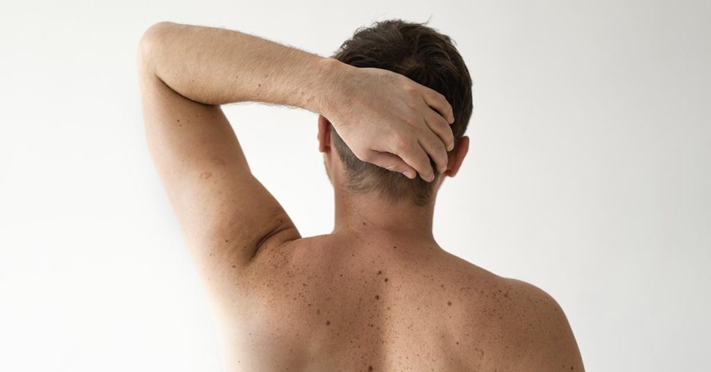 shirtless man seen from behind with arm raised with hand behind his head