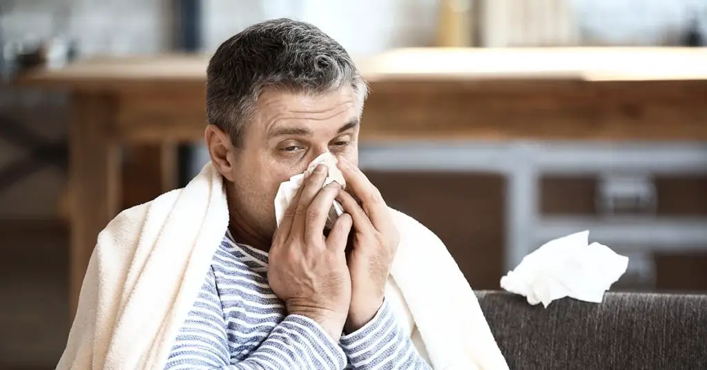 man blowing nose into tissue