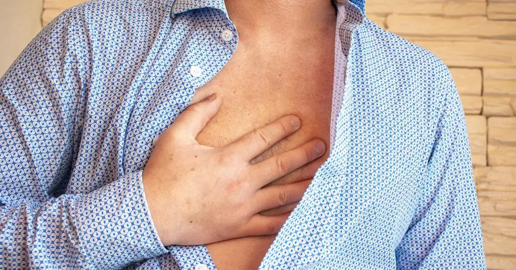 man with shirt unbuttoned holding chest