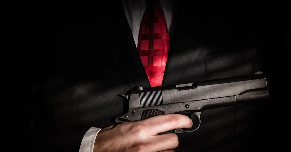 person holding gun to chest with red tie