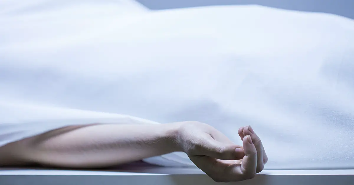 body in gown laying in on a metal table in what is most likely a morgue