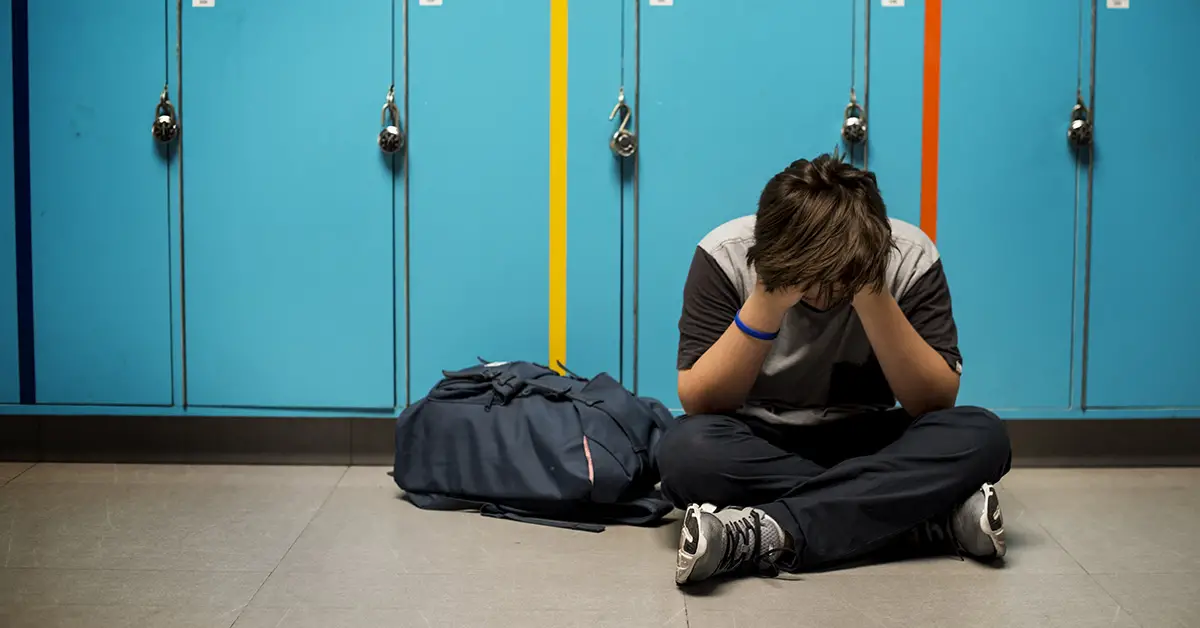 student in dismay sitting in the hallway against a locker