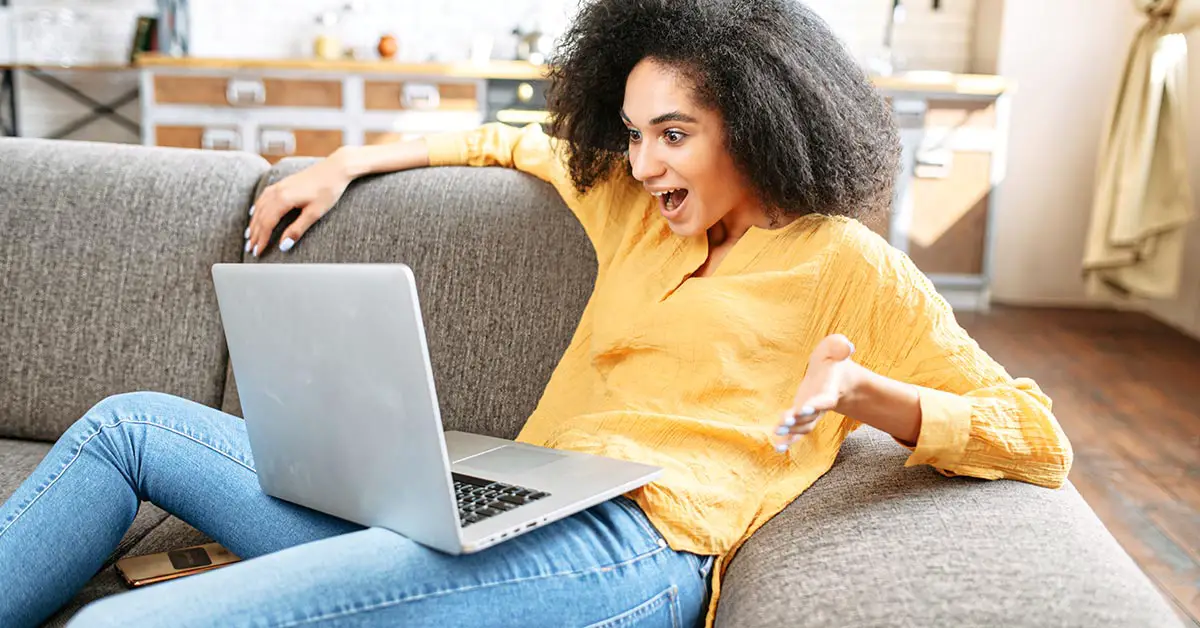 excited woman using laptop on couch