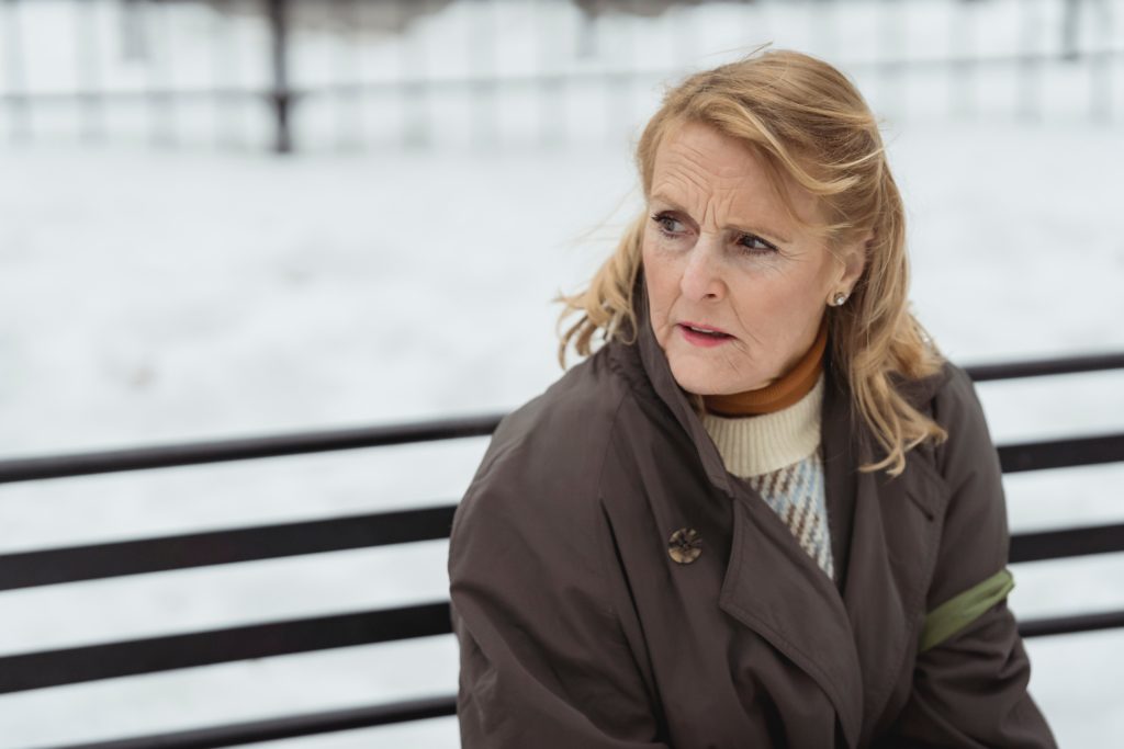 photo of a sad older woman sitting outside in the snow