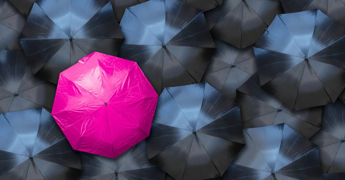 one pink umbrella in a group of many black umbrellas seen from above