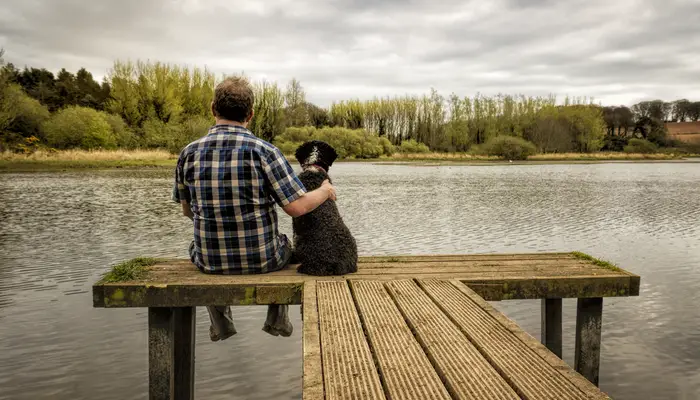 a man sitting on the end of a dock with his dog