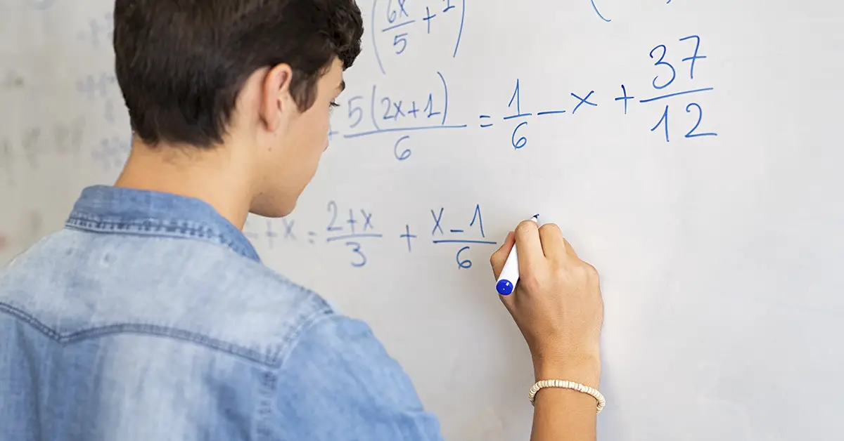 teen boy writing math equations on whiteboard in blue marker