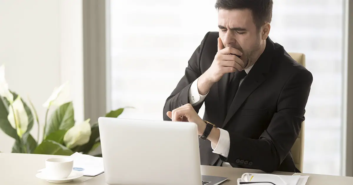 man yawning at work while sitting at desk using laptop