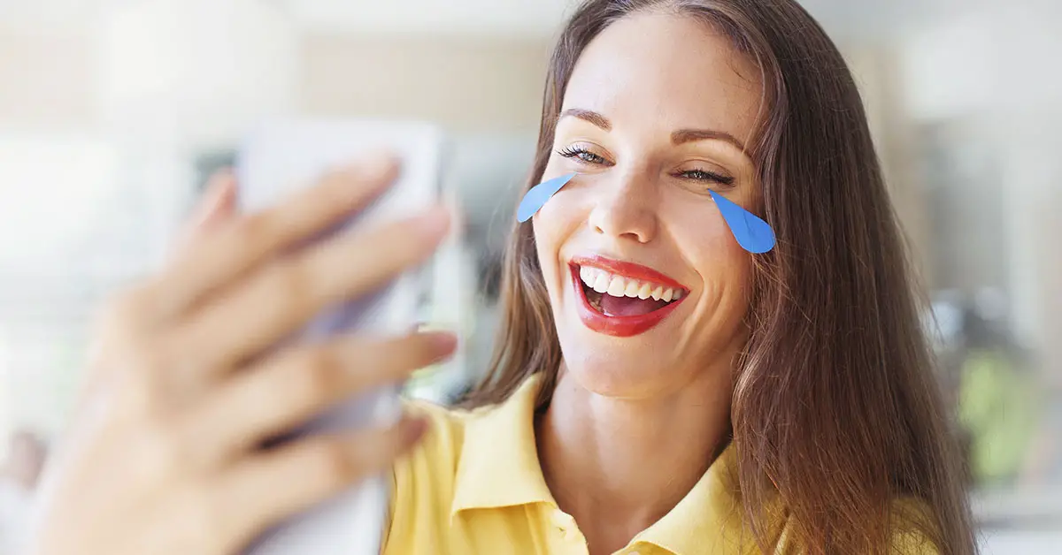 woman laughing while using smartphone. She has illustrated cartoon tears coming from here eyes meant to resemble the "crying laughing" emoji