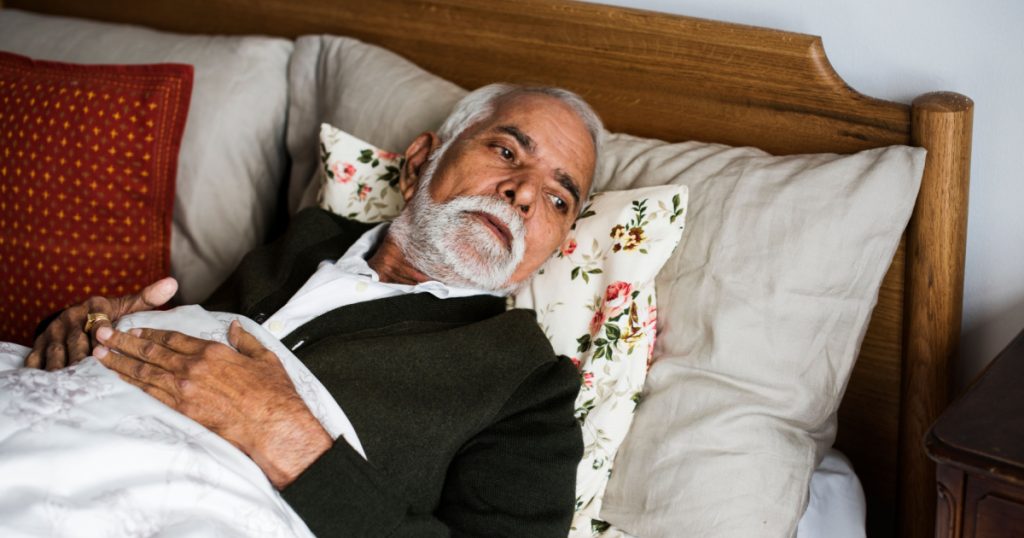 An elderly Indian man in bed at retirement home