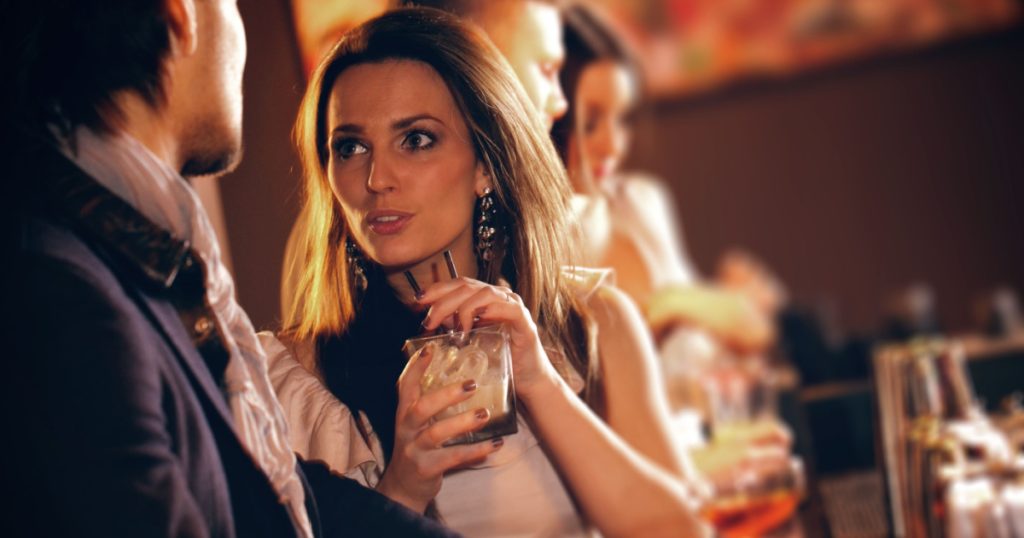 Young woman with a glass of wine talking to a man at the bar
