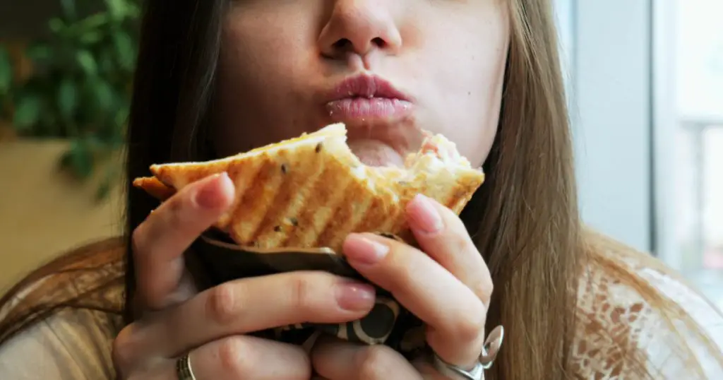 Close-up portrait of young hungry woman with pleasure eats crisp toast in a cafe, fast food restaurant
