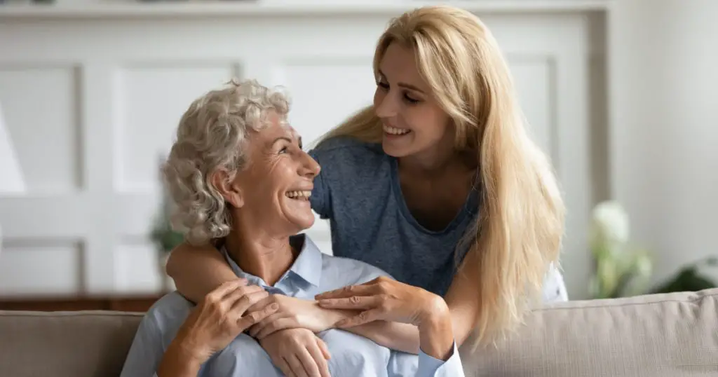 Overjoyed senior 60s mother and adult daughter relax together in living room hugging and cuddling, happy mature mum and grownup girl embrace show love enjoy home family weekend together
