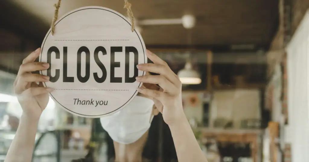 Closed. waitress woman wearing protection face mask turning close sign board on glass door in modern cafe coffee shop, cafe restaurant, retail store, small business owner, food and drink concept
