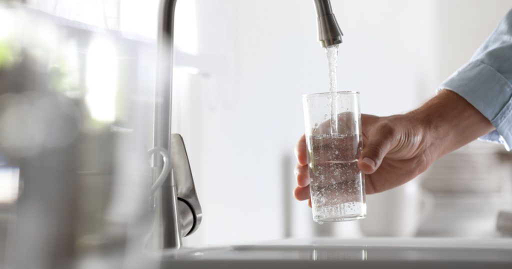 Man pouring water into glass in kitchen, closeup
