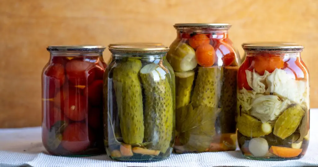 Glass jars with pickled cucumbers (pickles), pickled tomatoes and cabbage. Jars of various pickled vegetables. Canned food in a rustic composition.
