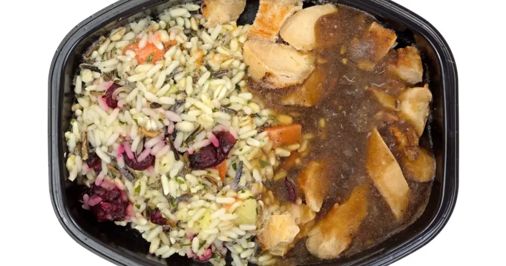 A top view of a rice and turkey with gravy TV dinner in a black tray.
