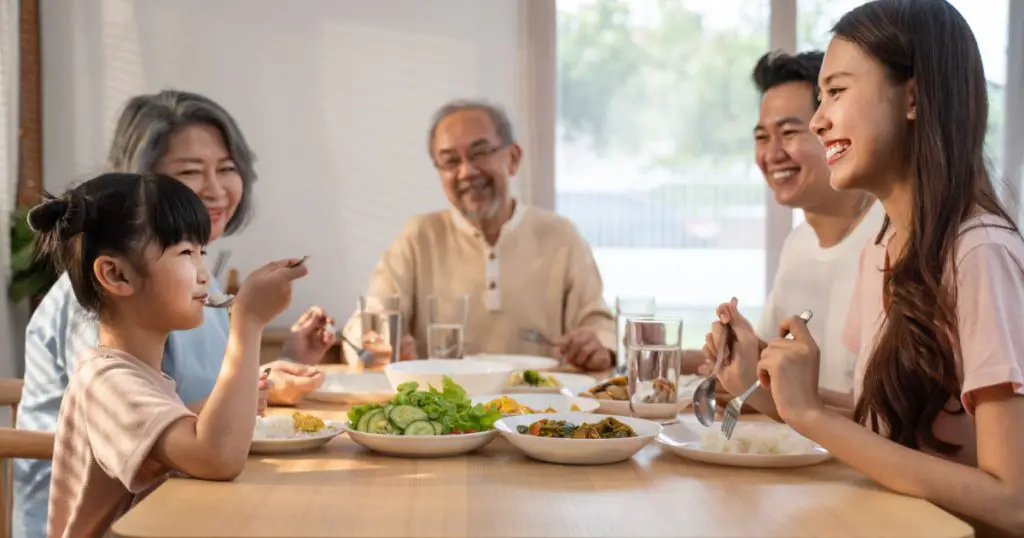 Big Asian happy family spend time having lunch on dinner table together. little kid daughter enjoy eating food with father, mother and grandparents. Multi-Generation relationship and activity in house
