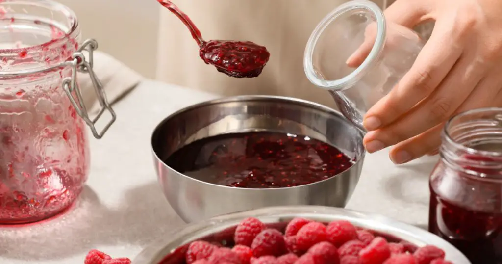 Woman making sweet raspberry jam, closeup
