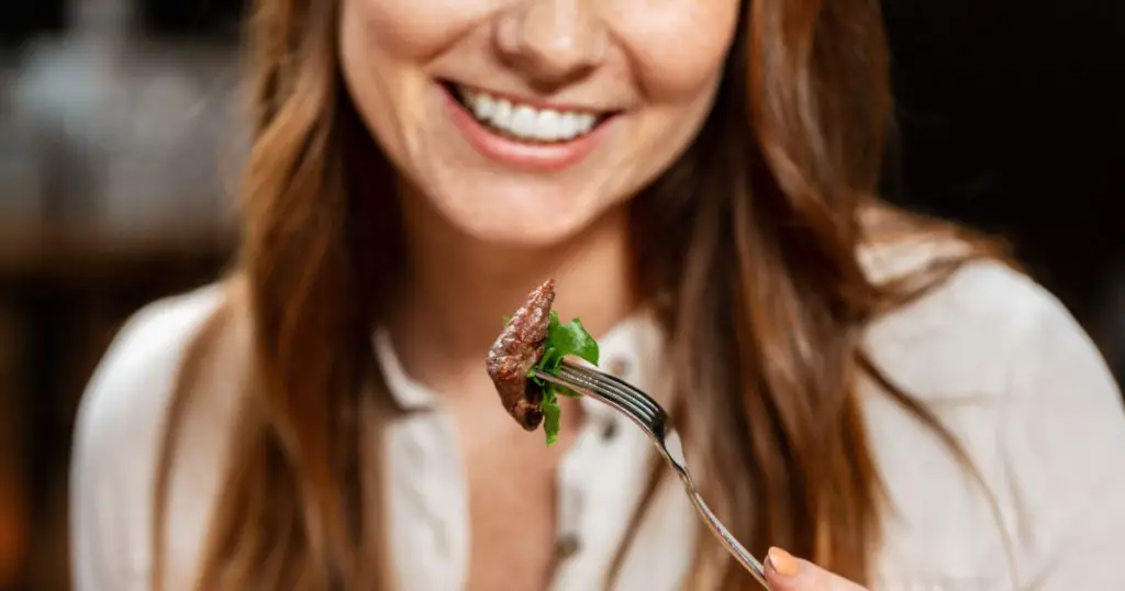 food, people and leisure concept - close up of happy smiling woman eating meat for lunch at restaurant
