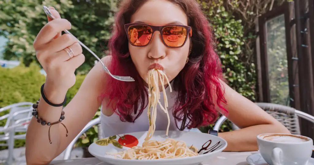 The girl is in a funny hurry and eats Italian pasta in a cafe. The concept of good manners and rules of etiquette on the first date
