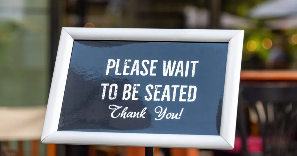 Please wait to be seated sign standing at the front of a restaurant. 