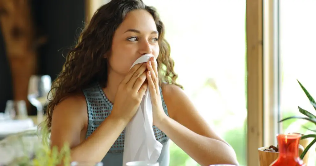 Woman cleaning mouth with a napkin sitting in a restaurant
