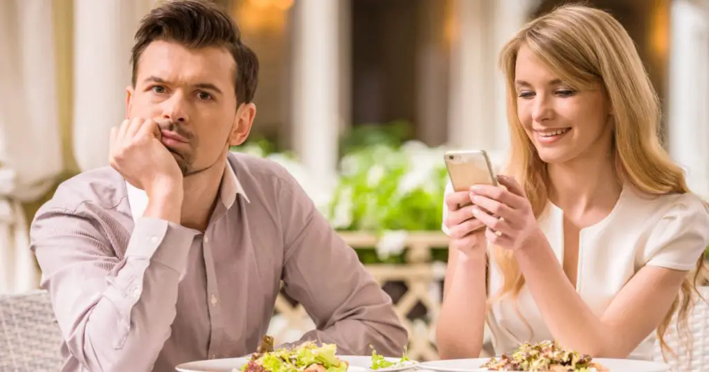 Man is getting bored in restaurant while his woman looking at phone.
