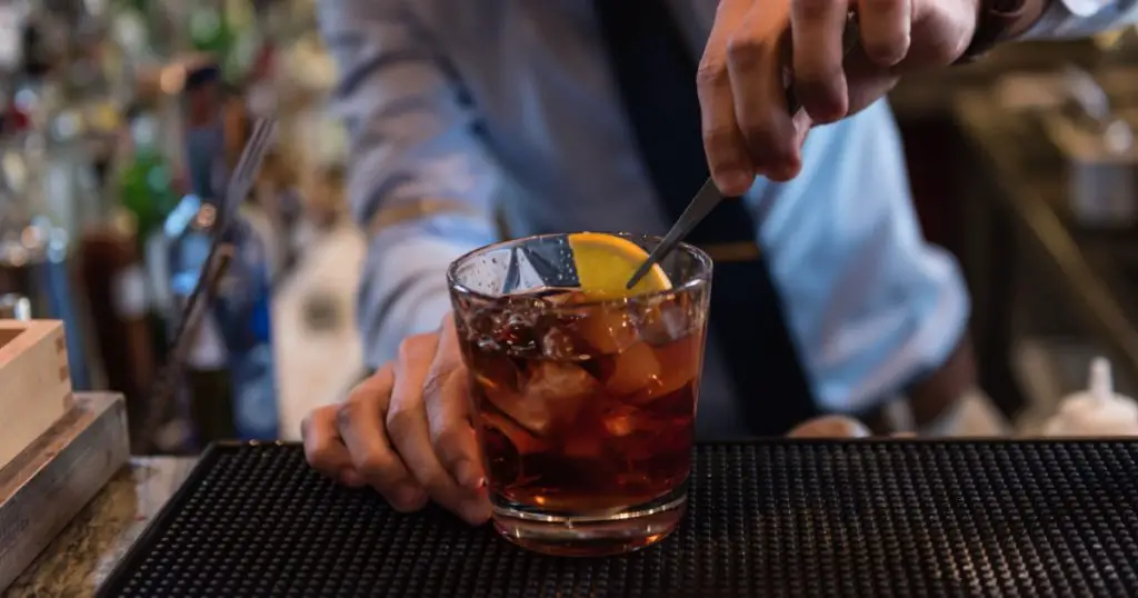 Bartender in formal dress is serving cocktail drinks behind bar counter

