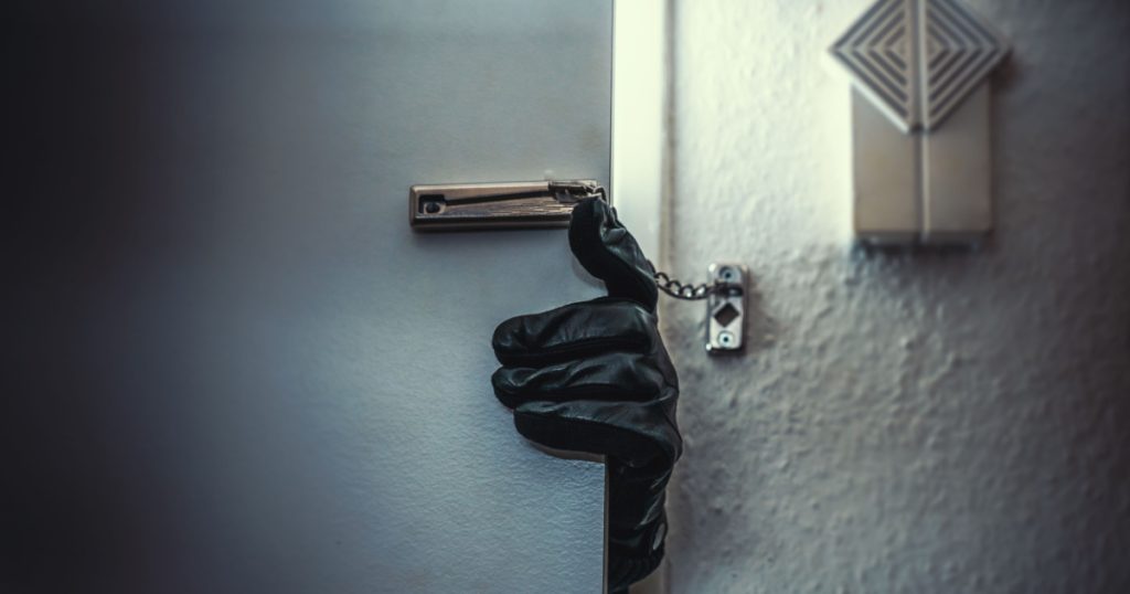masked burglar with crowbar breaking and entering into a victim's home