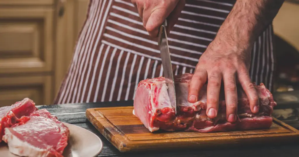 Man cuts of fresh piece of meat on a wooden cutting board in the home kitchen
