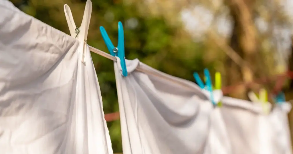White clothes hung out to dry on a washing line and fastened by the clothes pegs in the bright warm sunny day. Blurred garden at background.
