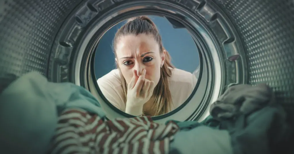 Woman staring at the laundry in the washing machine and holding her nose
