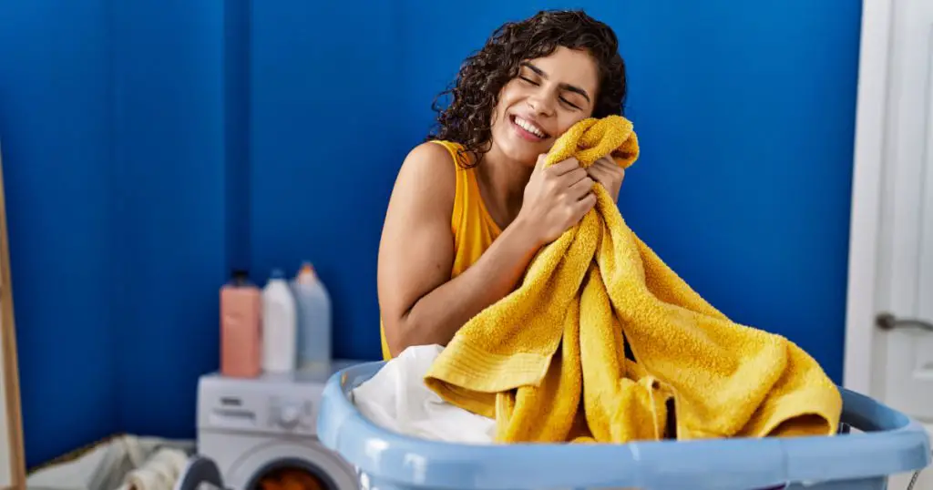 Young latin woman smiling confident touching face with soft towel at laundry room
