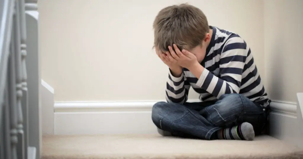 Upset problem child with head in hands sitting on staircase concept for bullying, depression stress or frustration
