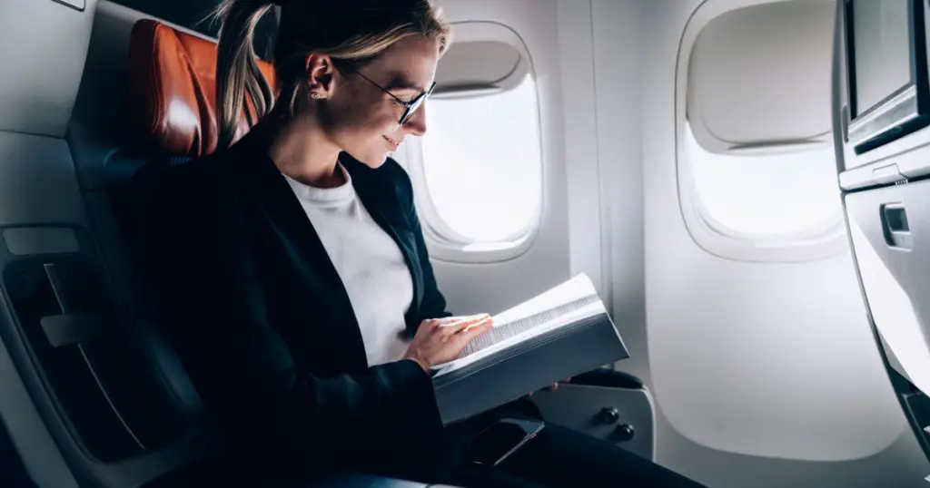 Successful female book editor reading literature during time in airplane before business meeting with writer, confident formally dressed woman enjoying international flight and leisure for novel
