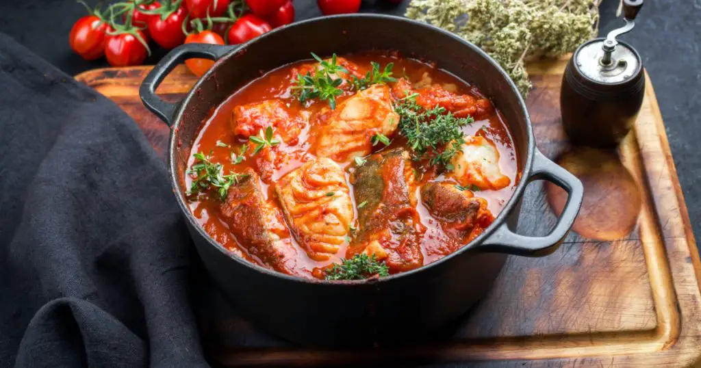 Traditional Brazilian fish stew moqueca baiana with fish filet in tomato sauce as closeup in a modern design cast-iron roasting dish
