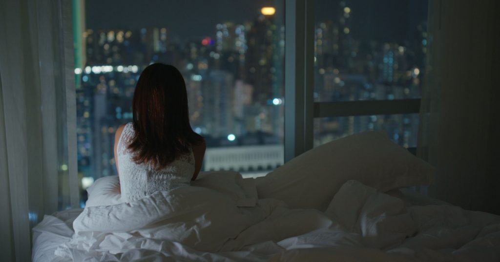 Woman look at the city view and lying on bed at night
