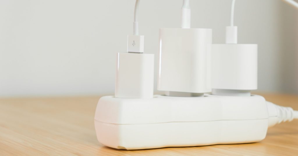 The electrical extension strip with connected white power plugs on the wooden table. Smartphones chargers in power strip for electrical sockets
