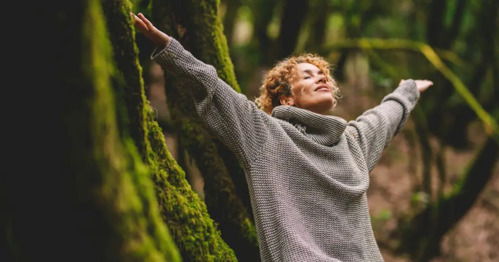 Overjoyed happy woman enjoying the green beautiful nature woods forest around her - concept of female people and healthy natural lifestyle - happiness emotion and adult lady opening arms
