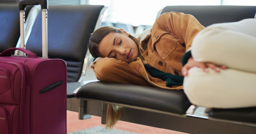 Tired, sleeping and woman at airport, waiting and bench for travel, international transport and flight delay. Tourist nap on chair at airplane lounge before journey with baggage, luggage and suitcase
