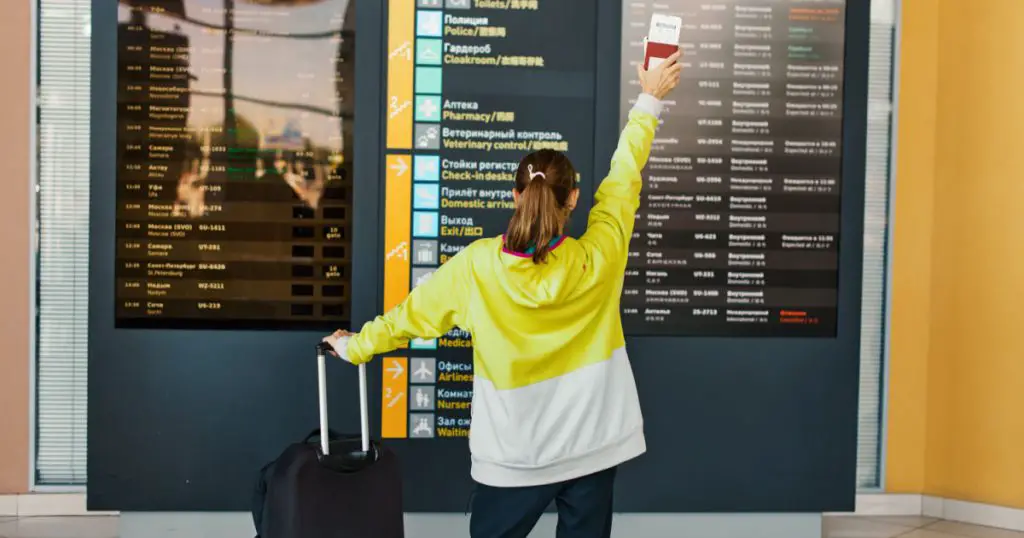 woman holding in hands passport and ticket to fly away, traveler standing in front of information board in airport in Russian city of Yekaterinburg. Concept of traveling People from behind
