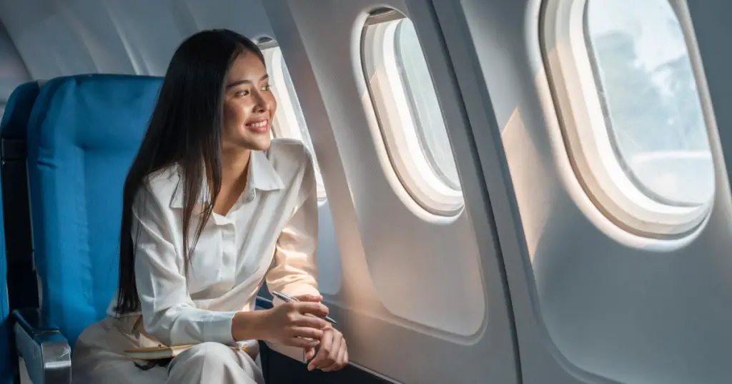 Asian woman sitting in a seat in airplane and looking out the window going on a trip vacation travel concept
