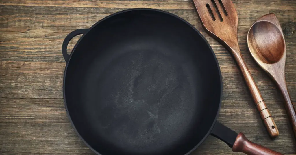 New Clean Empty Cast Iron Frying Pan And Spatula Top View On The Wooden Background
